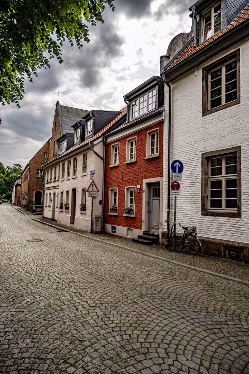 Cobblestone street with historic european buildings under a cloudy sky.