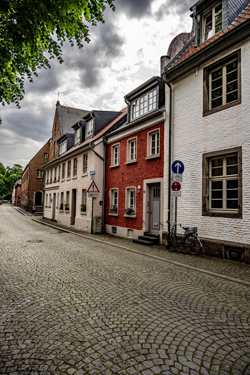 Cobblestone street with historic european buildings under a cloudy sky.